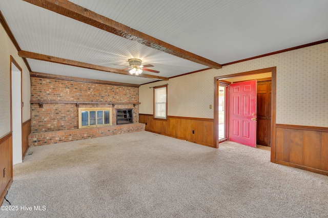 unfurnished living room with wallpapered walls, a brick fireplace, beamed ceiling, and wainscoting