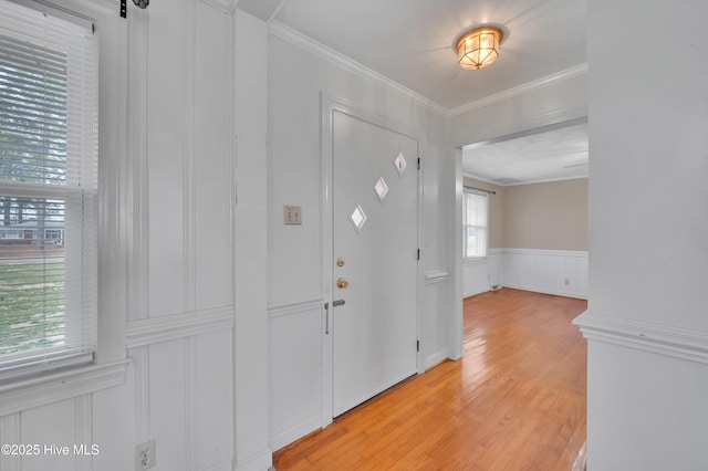 entrance foyer featuring ornamental molding, wainscoting, light wood-style floors, and a decorative wall