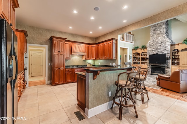 kitchen with black refrigerator with ice dispenser, kitchen peninsula, a kitchen breakfast bar, a stone fireplace, and light hardwood / wood-style floors