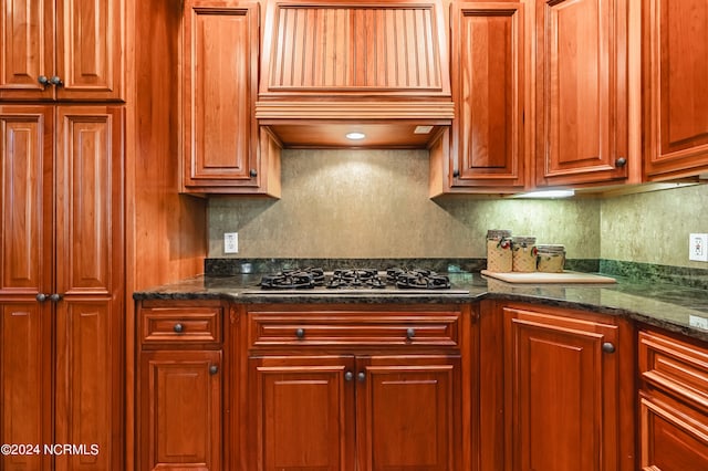 kitchen with stainless steel gas cooktop, premium range hood, decorative backsplash, and dark stone counters