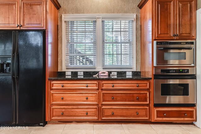 kitchen featuring dark stone countertops, light tile patterned floors, and black fridge