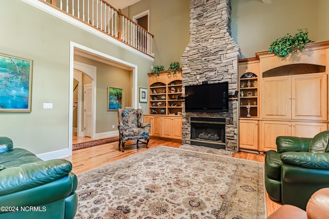 living room with hardwood / wood-style flooring, a towering ceiling, built in features, and a stone fireplace