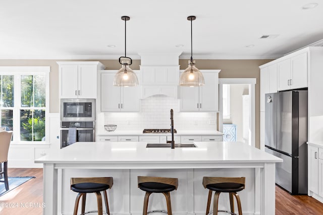 kitchen featuring pendant lighting, decorative backsplash, an island with sink, appliances with stainless steel finishes, and white cabinetry