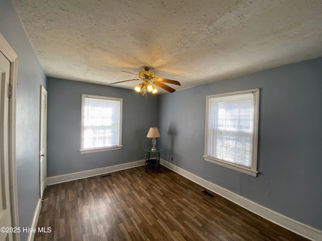 empty room with a textured ceiling, dark wood-style flooring, visible vents, and baseboards