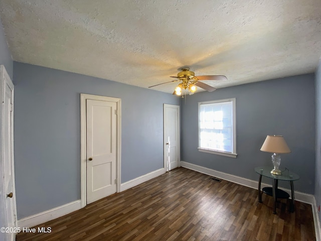 unfurnished bedroom featuring dark wood-type flooring, visible vents, a textured ceiling, and baseboards