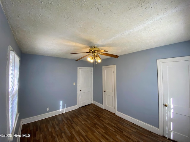 empty room with dark wood-style floors, a textured ceiling, and baseboards