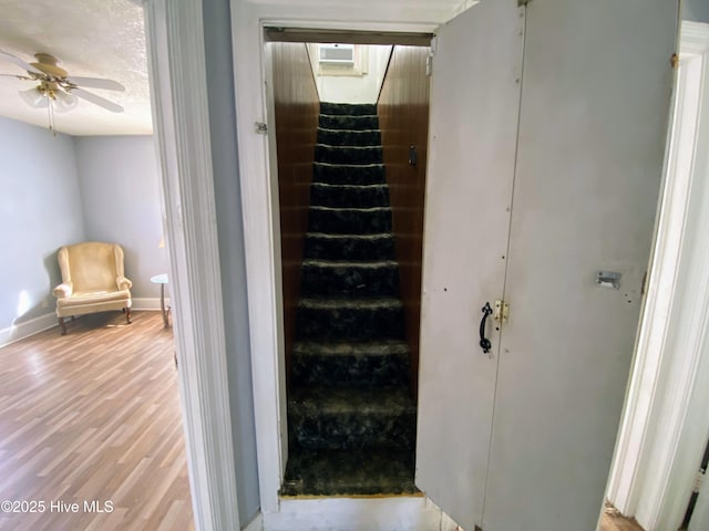 stairs featuring ceiling fan, a textured ceiling, baseboards, and wood finished floors