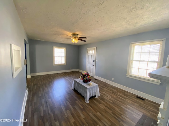 interior space with a textured ceiling, dark wood-type flooring, visible vents, and baseboards