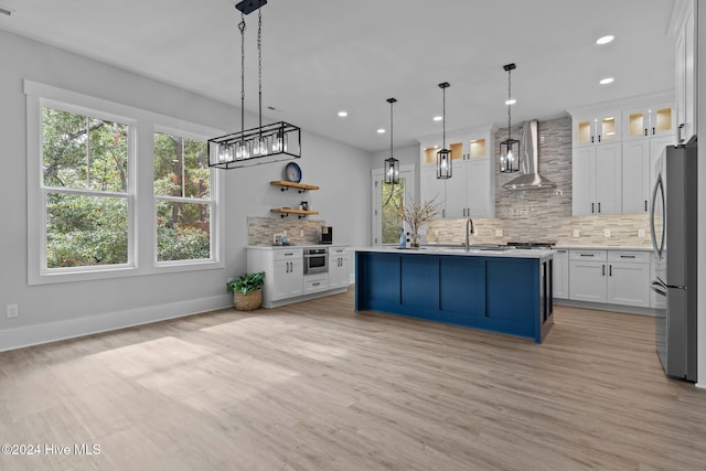 kitchen with white cabinets, wall chimney range hood, decorative backsplash, decorative light fixtures, and stainless steel refrigerator