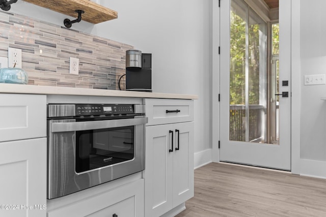 kitchen with decorative backsplash, white cabinets, oven, and a healthy amount of sunlight