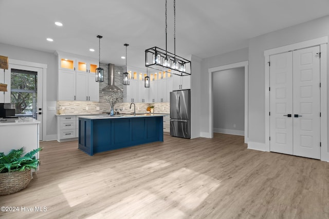 kitchen featuring decorative backsplash, stainless steel fridge, wall chimney exhaust hood, white cabinets, and hanging light fixtures