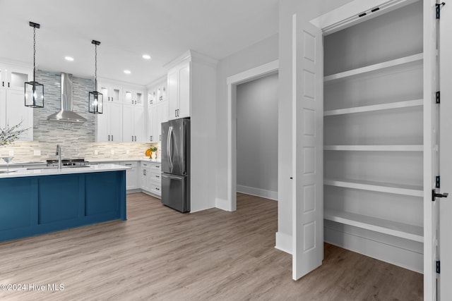 kitchen featuring built in features, white cabinetry, stainless steel refrigerator, and wall chimney range hood