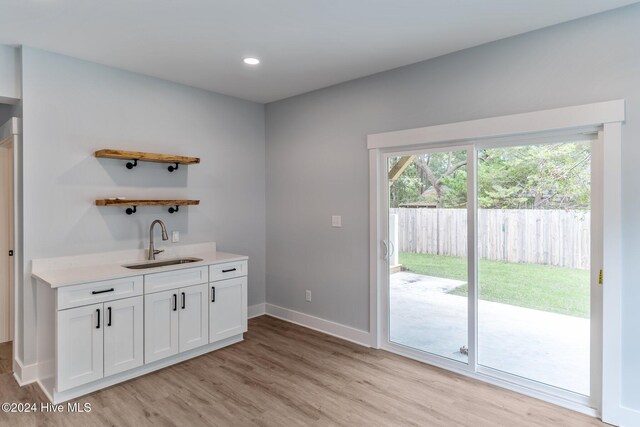 bar featuring white cabinets, light hardwood / wood-style flooring, and sink