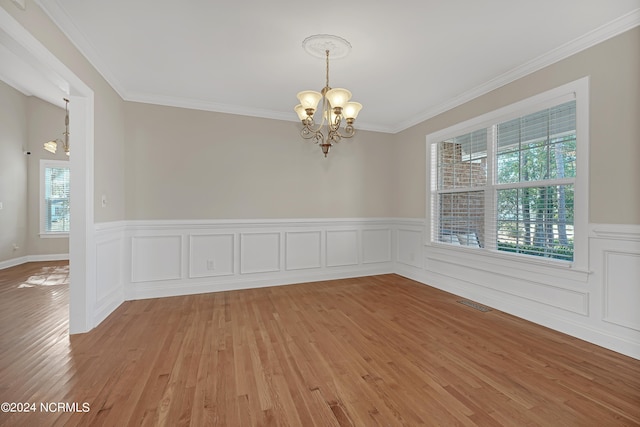 unfurnished room featuring a notable chandelier, a healthy amount of sunlight, ornamental molding, and light hardwood / wood-style flooring