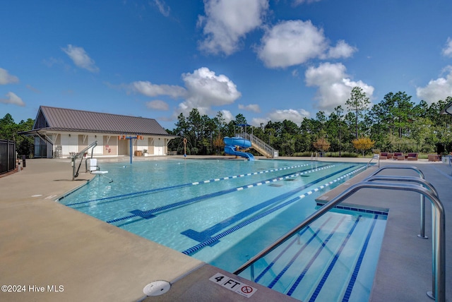 view of swimming pool with a patio, an outdoor structure, and a water slide