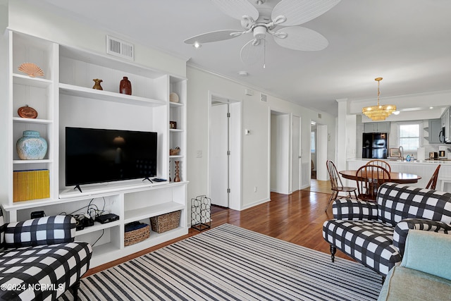 living room with built in features, ceiling fan with notable chandelier, crown molding, dark wood-type flooring, and sink