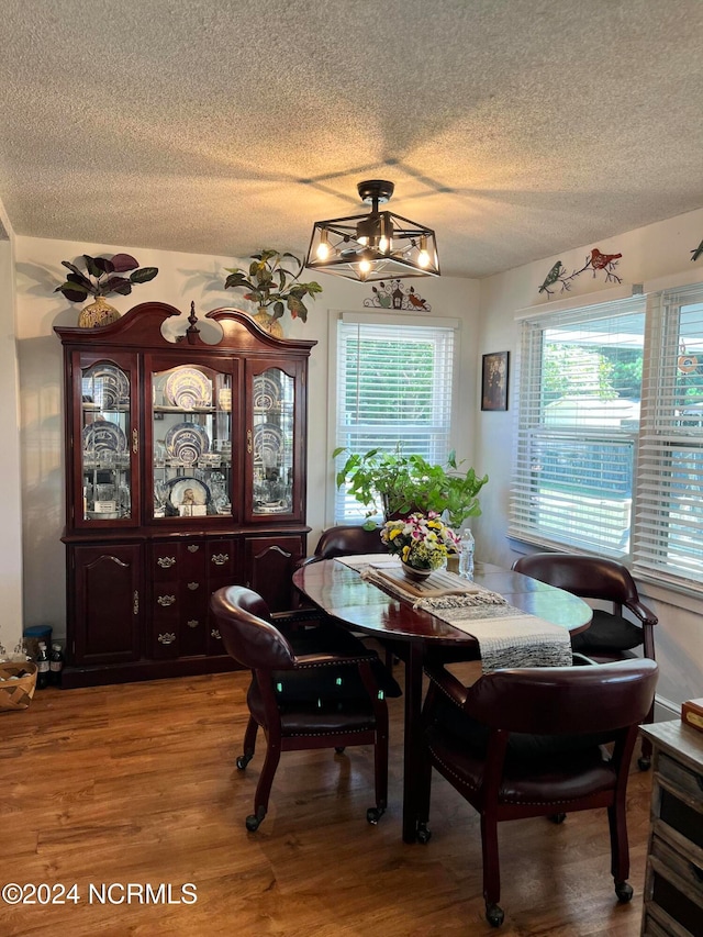 dining room with wood-type flooring, a textured ceiling, and an inviting chandelier