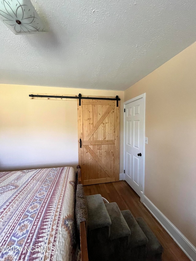 bedroom featuring a barn door, hardwood / wood-style flooring, and a textured ceiling