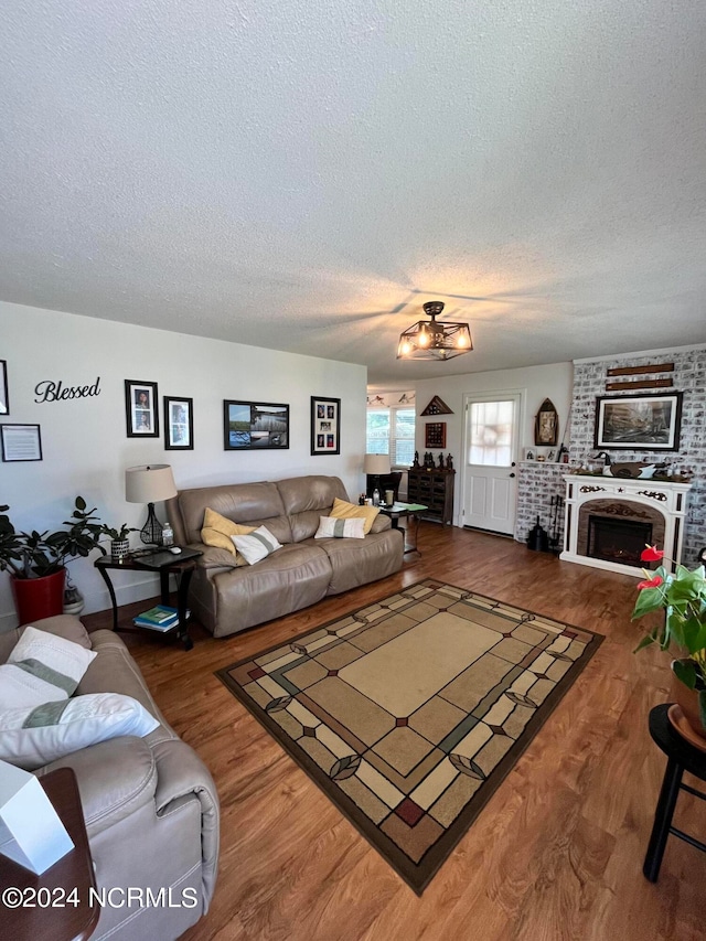 living room featuring wood-type flooring, a textured ceiling, and a brick fireplace