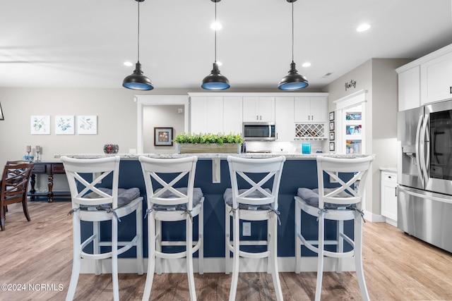 kitchen featuring a center island with sink, white cabinetry, stainless steel appliances, and light wood-type flooring