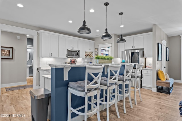 kitchen featuring appliances with stainless steel finishes, an island with sink, hanging light fixtures, white cabinetry, and light hardwood / wood-style floors