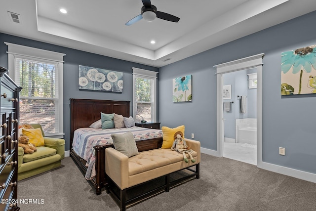 carpeted bedroom featuring multiple windows, ensuite bathroom, a raised ceiling, and ceiling fan