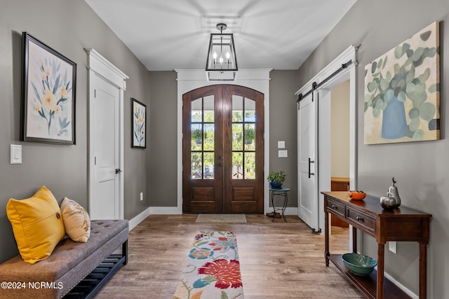 entryway featuring french doors, a barn door, light hardwood / wood-style flooring, and an inviting chandelier