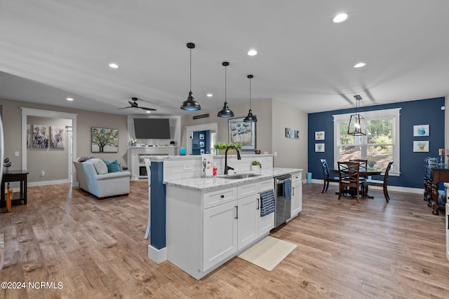 kitchen with dishwasher, a center island with sink, sink, decorative light fixtures, and white cabinetry