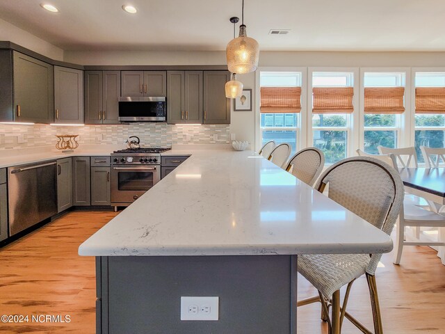 kitchen with light hardwood / wood-style floors, decorative backsplash, decorative light fixtures, and stainless steel appliances