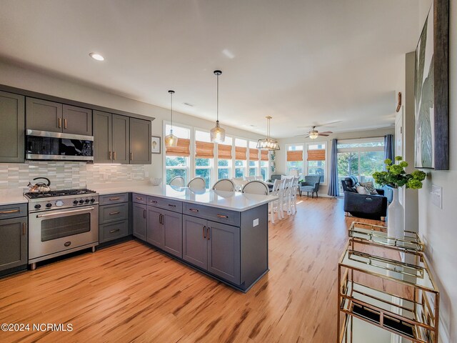 kitchen with light hardwood / wood-style floors, gray cabinets, kitchen peninsula, hanging light fixtures, and appliances with stainless steel finishes