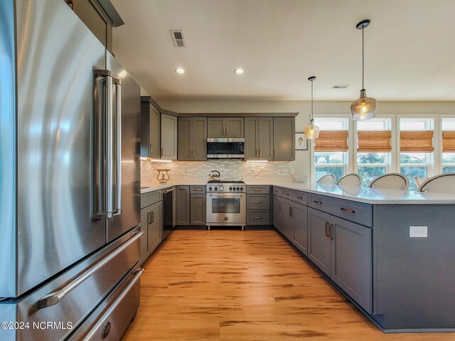 kitchen featuring light wood-type flooring, high quality appliances, hanging light fixtures, and gray cabinets