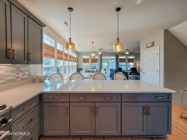 kitchen with ceiling fan, pendant lighting, gray cabinetry, backsplash, and light wood-type flooring