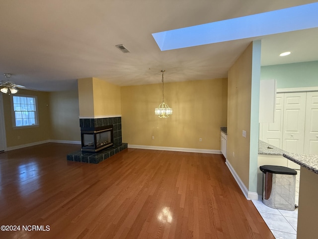 unfurnished living room with light hardwood / wood-style flooring, ceiling fan with notable chandelier, and a skylight