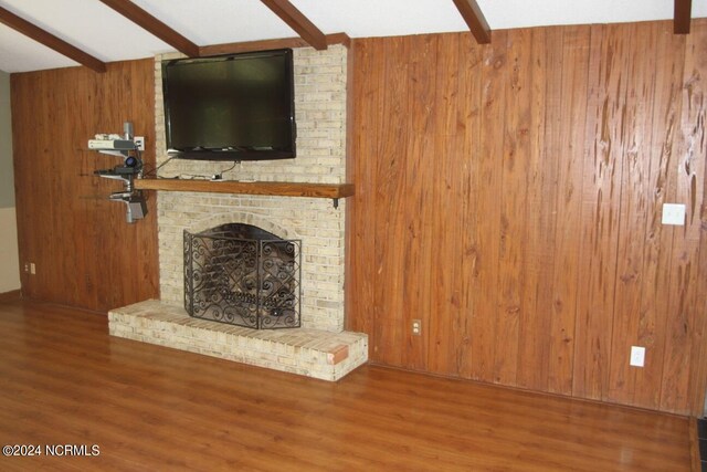 unfurnished living room featuring beam ceiling, wood-type flooring, a fireplace, and wooden walls