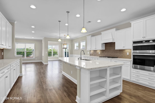 kitchen featuring pendant lighting, stainless steel double oven, a center island with sink, sink, and white cabinets