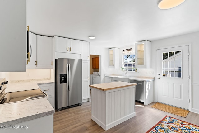 kitchen featuring washer and dryer, light wood-type flooring, a kitchen island, white cabinetry, and stainless steel appliances