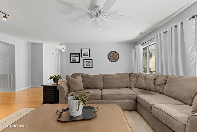 living room with ceiling fan, a textured ceiling, and light hardwood / wood-style floors