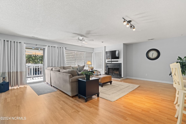 living room with light wood-type flooring, ceiling fan, and a textured ceiling