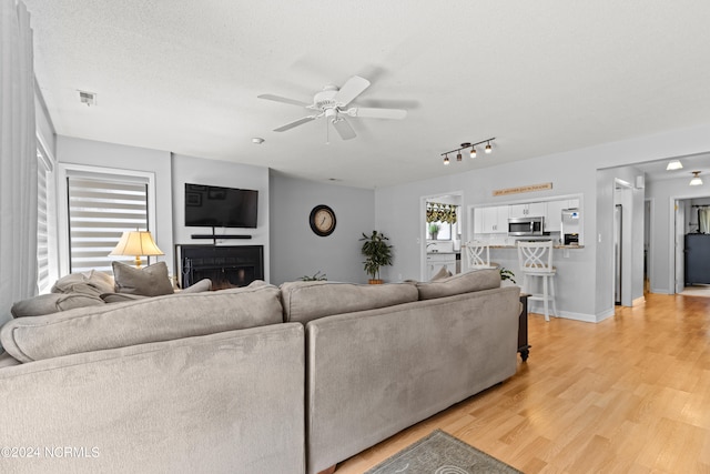 living room featuring ceiling fan, a textured ceiling, and light hardwood / wood-style flooring