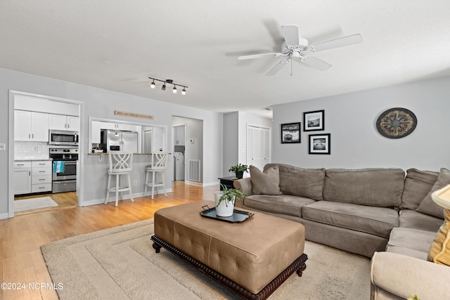 living room with light wood-type flooring, ceiling fan, and a textured ceiling