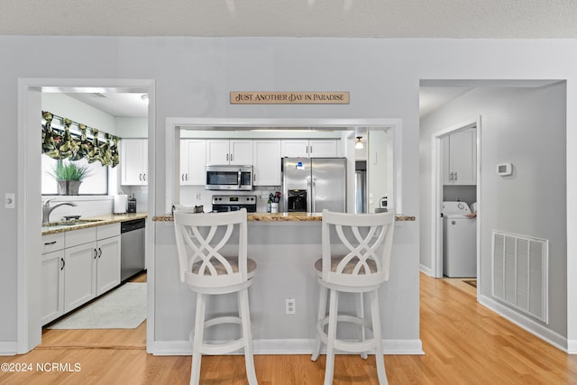 kitchen with light wood-type flooring, sink, washer / dryer, stainless steel appliances, and white cabinetry