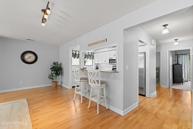 kitchen with light hardwood / wood-style flooring, kitchen peninsula, white cabinets, and a kitchen bar