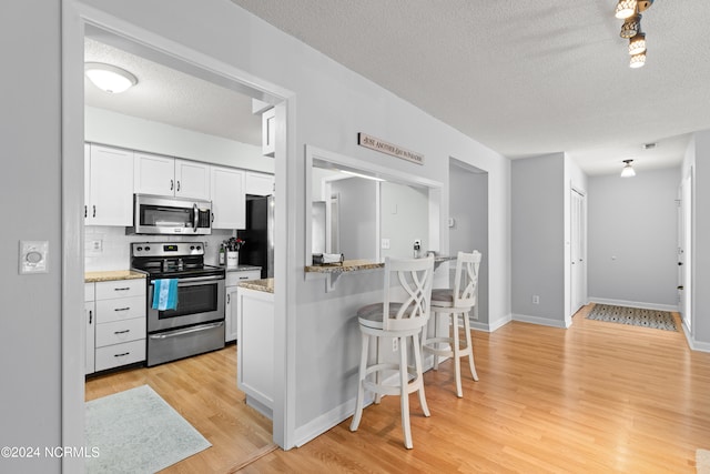 kitchen featuring light wood-type flooring, light stone counters, white cabinets, appliances with stainless steel finishes, and a textured ceiling