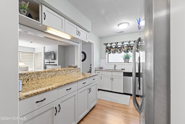 kitchen featuring sink, a textured ceiling, white cabinetry, appliances with stainless steel finishes, and light hardwood / wood-style floors