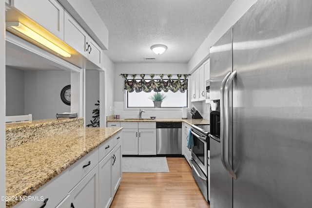 kitchen featuring light wood-type flooring, light stone counters, stainless steel appliances, white cabinets, and a textured ceiling