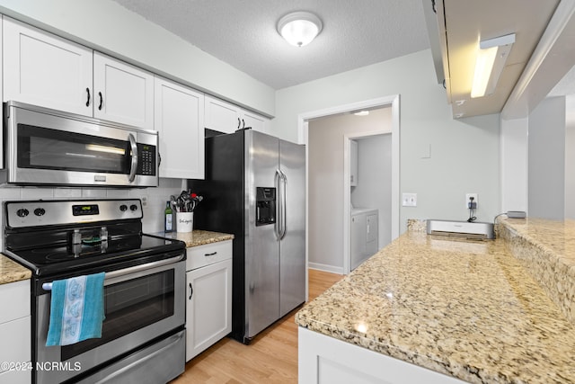 kitchen with stainless steel appliances, light wood-type flooring, washer and dryer, and white cabinetry