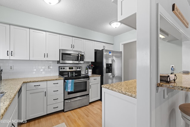 kitchen featuring light hardwood / wood-style flooring, stainless steel appliances, light stone countertops, backsplash, and white cabinets