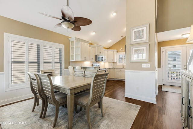 dining area with a wainscoted wall, high vaulted ceiling, dark wood-type flooring, and a ceiling fan