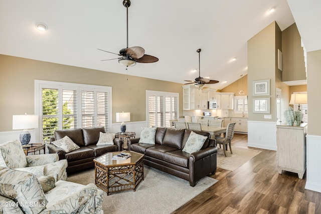 living area with wainscoting, high vaulted ceiling, ceiling fan, and wood finished floors