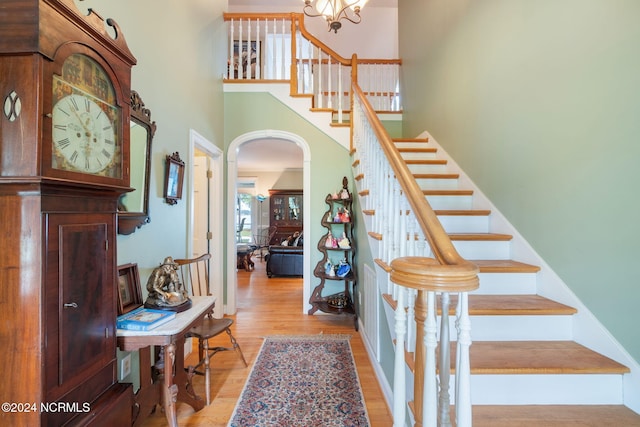 stairs featuring wood-type flooring, a high ceiling, and a notable chandelier